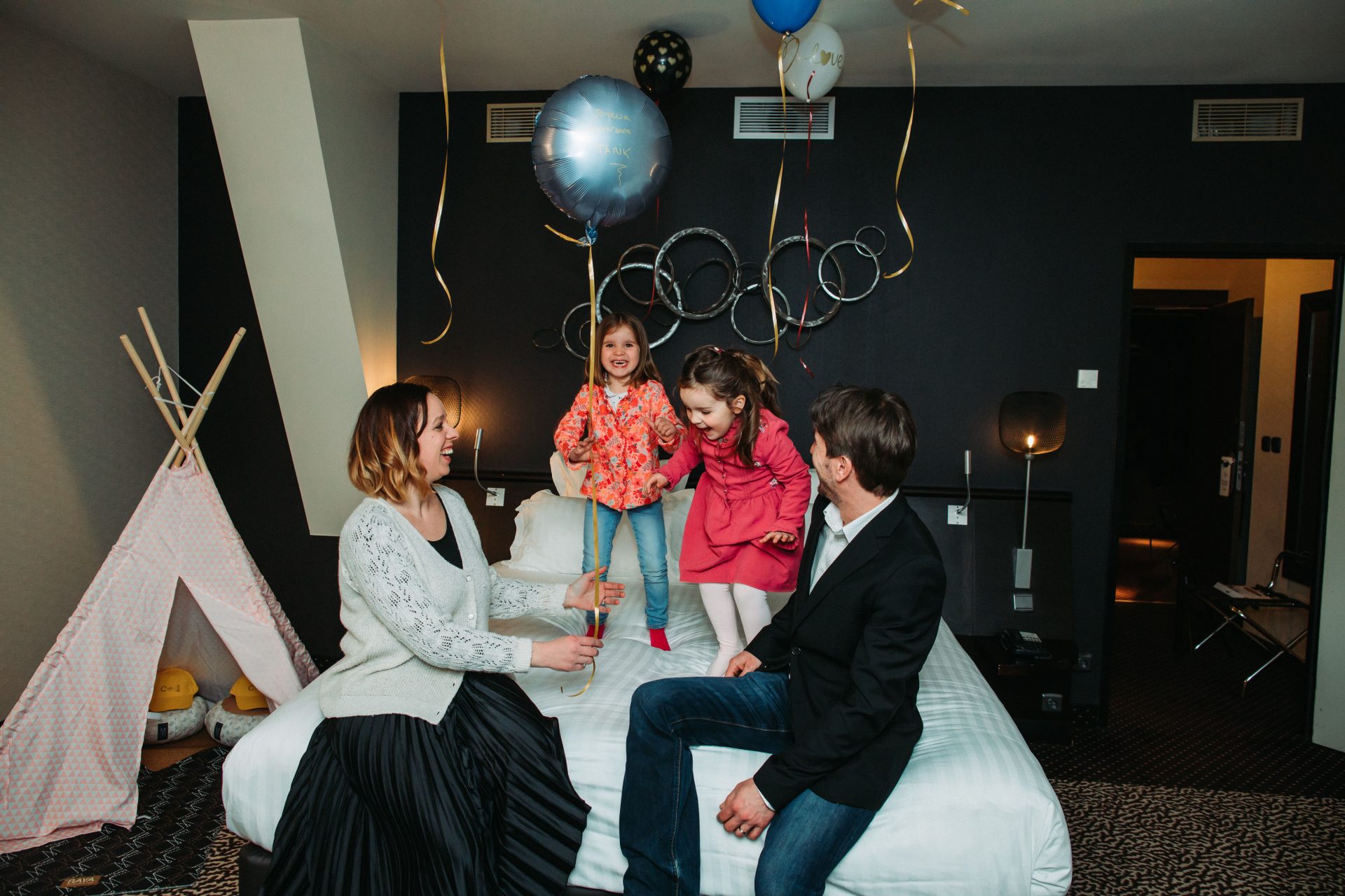 Photo d'entreprise d'une famille dans une chambre d'hôtel, avec des enfants qui sautent sur le lit